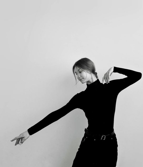 Person in a dynamic but controlled movement pose in a minimalist studio.
